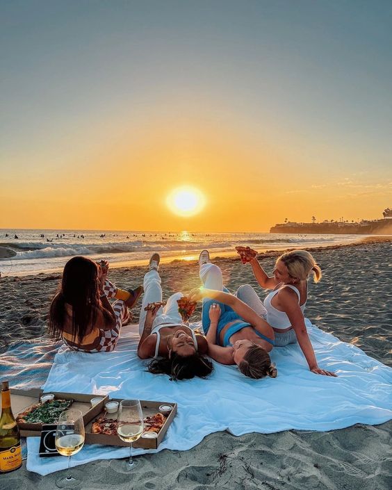 Gruppo ragazze alla pari al tramonto che fanno un picnic in spiaggia. 