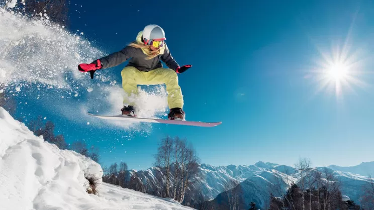 Ragazza che salta con lo snowboard in un fuori pista in montagna con la neve 